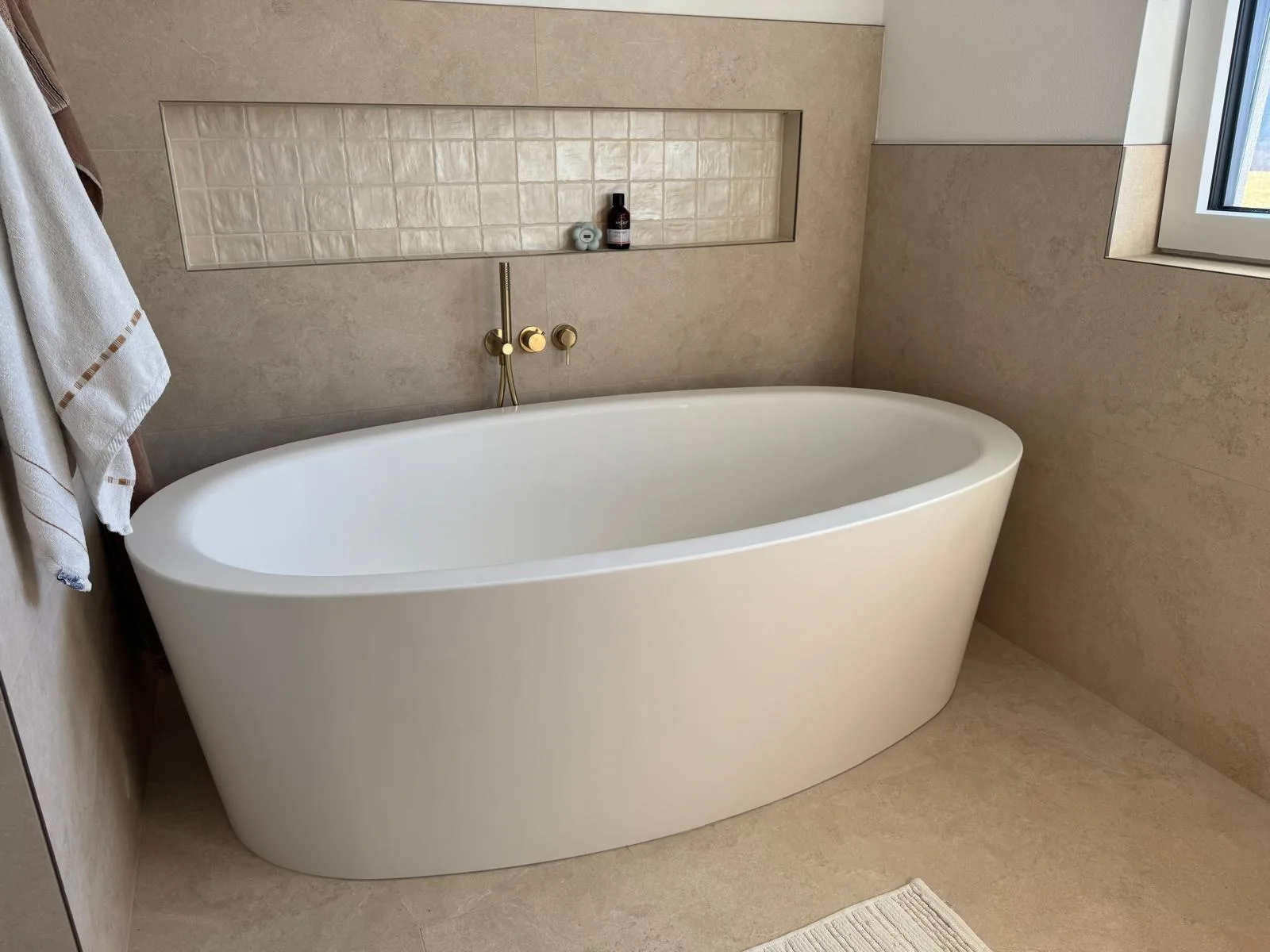 Badewanne unter einer gefliesten Nische, daneben ein Handtuch