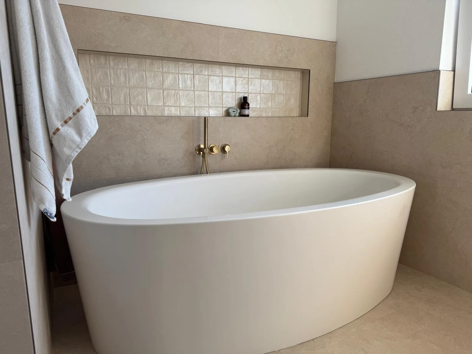 Freistehende Badewanne vor einer gefliesten Nische mit Ablage, Arbeit von Wilhelm Brugger