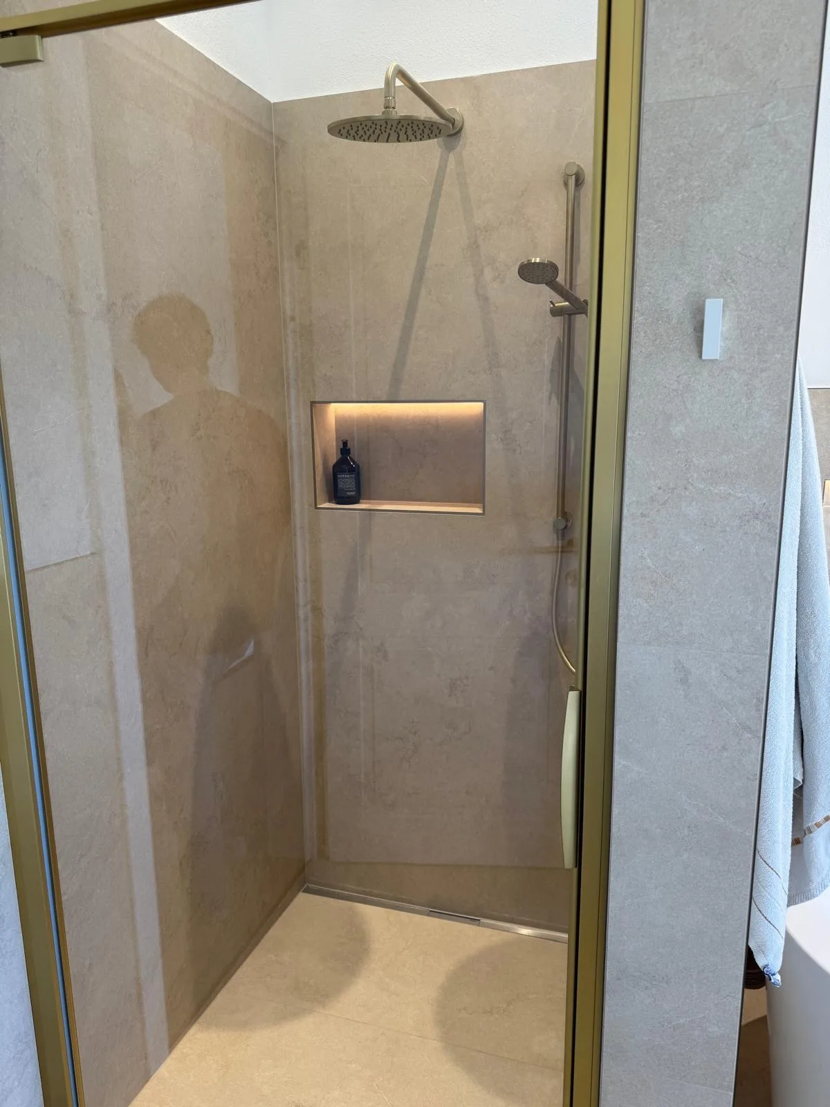 Begehbare Dusche mit Regenbrause und beleuchteter Ablagenische hinter einer Glastür