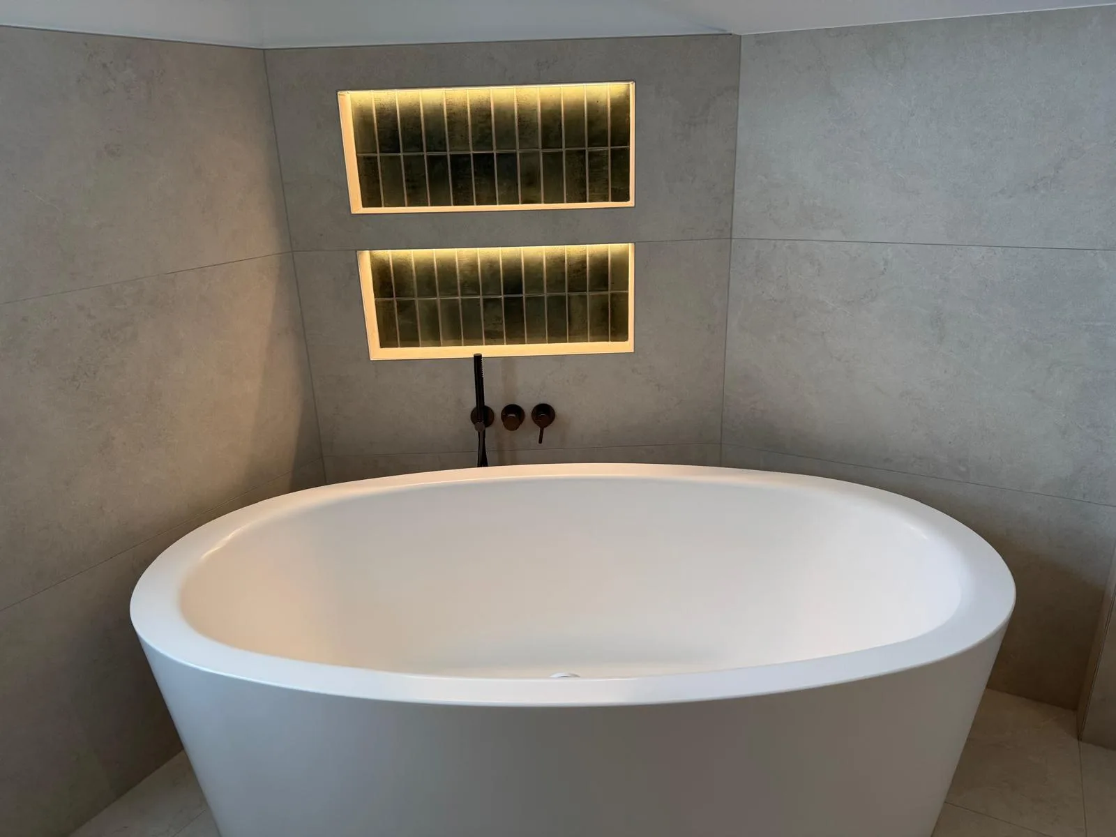 Freistehende weiße Badewanne vor zwei beleuchteten Wandnischen