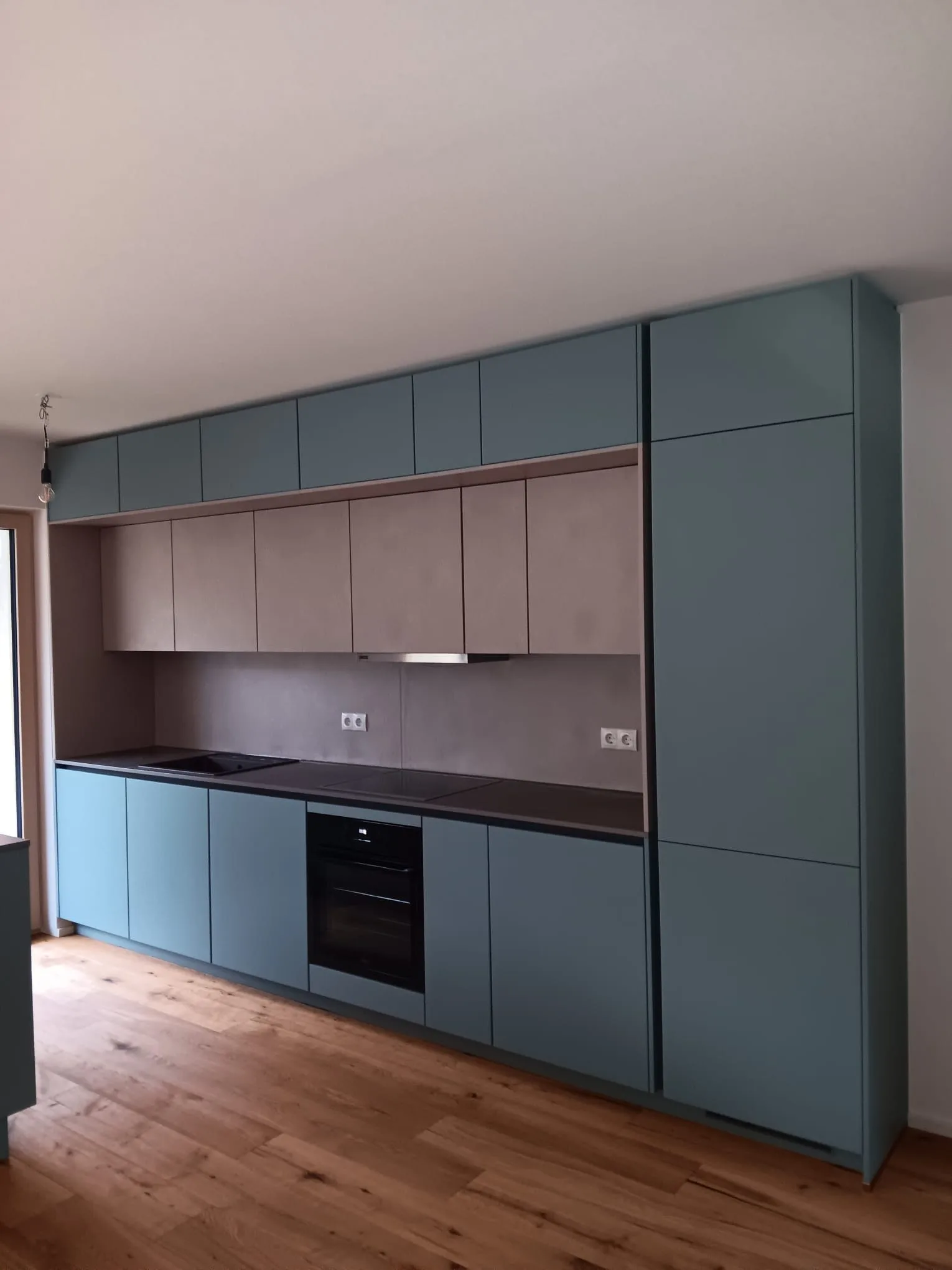 Küchenzeile mit blaugrünen und braunen Fronten vor einem Holzboden