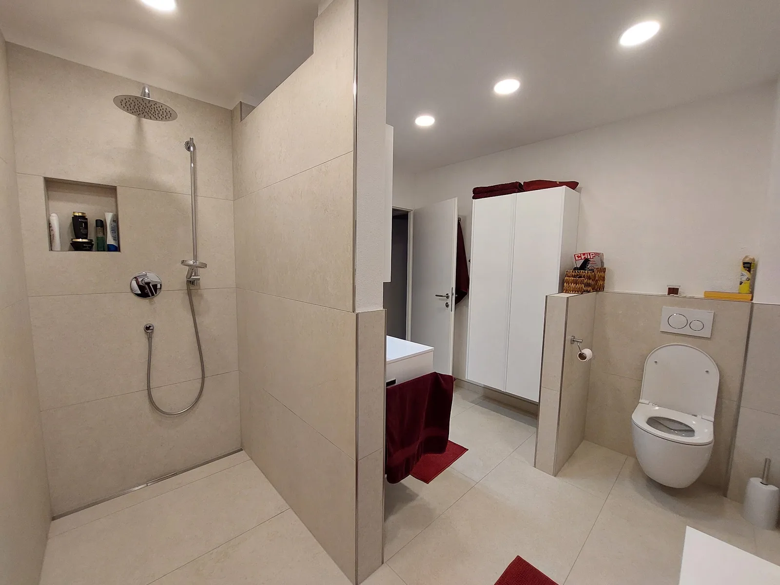 Saniertes Badezimmer mit bodengleicher Regendusche, Wand-WC und großformatigen beigen Fliesen